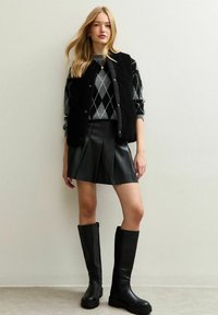 Zwart vest over een grijs argyle-jersey, geplooide zwarte leren rok en glanzende zwarte kniehoge laarzen. Glad texturen en gestroomlijnd ontwerp.