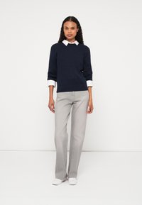 Jūras spēku zila adīta džemperis ar teksturētu rakstu, saskaņots ar gaiši pelēkiem taisnajiem biksēm un baltām apaviem. No džempera iznirst apkakles krekls.