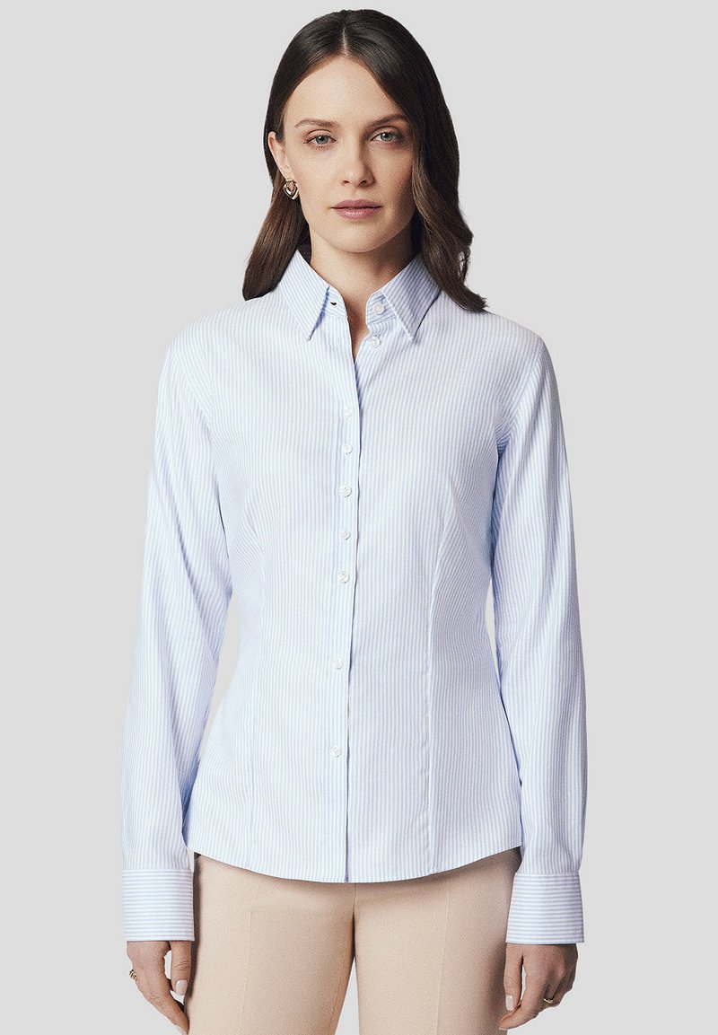 Jasnoniebieska koszula zapinana na guziki z pionowymi białymi paskami, dopasowany krój, długie rękawy i stożkowy kołnierzyk. Białe zapięcia na guziki z przodu.