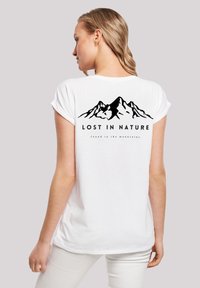 White cotton t-shirt featuring a black mountain graphic with the text "LOST IN NATURE" and "found in the mountains" on the back. Short sleeves.