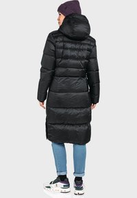 Schwarze, wattierte Jacke mit Kapuze, die horizontale Steppabschnitte aufweist. Kombiniert mit hellblauen Jeans und weißen Sneakers mit grünen und lila Akzenten.