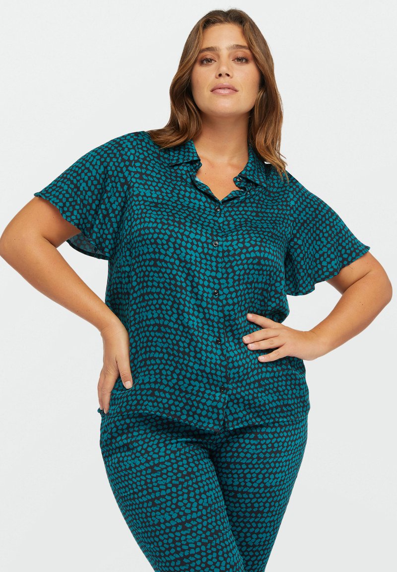 Camicia a maniche corte con bottoni e pantaloni abbinati in teal con un motivo a pois neri. Il tessuto è liscio e ha una consistenza leggermente trasparente.