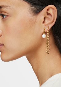 Pendientes de oro con una perla esférica colgante, adornados con una cadena de cuentas de oro alternadas, que exhiben un diseño elegante y moderno.