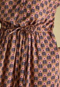 Braun bedrucktes Kleid mit floralen Mustern in Pink und Marineblau. Verfügt über einen geknöpften Oberteil und einen Bindegürtel, strukturierten Stoff mit Raffungen.