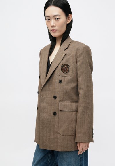 Blazer maro cu tip herringbone, având un design dublebreasted, nasturi negri și un buzunar pe piept cu un emblema brodată.