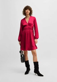 Short-sleeved, V-neck dress in glossy magenta fabric, featuring a gathered waist and flowing skirt, paired with knee-high black boots.