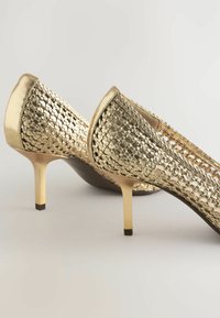 Guld, vävda högklackade skor med spetsig tå. Har en metallisk finish och en smal stilettklack med ett texturerat mönster.