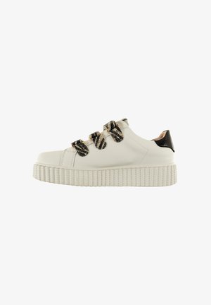 Zapatilla de piel blanca con acentos de rayas negras y doradas, suela texturizada y chunky, punta redondeada y detalle en charol negro en el talón.