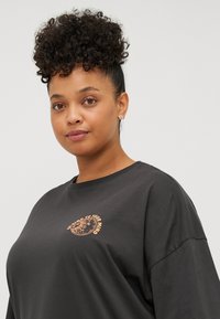 Schwarzes T-Shirt aus Baumwolle mit rundem Halsausschnitt und kurzen Ärmeln. Bedruckte Grafik in Hellbraun auf der Brust. Glatte Textur.