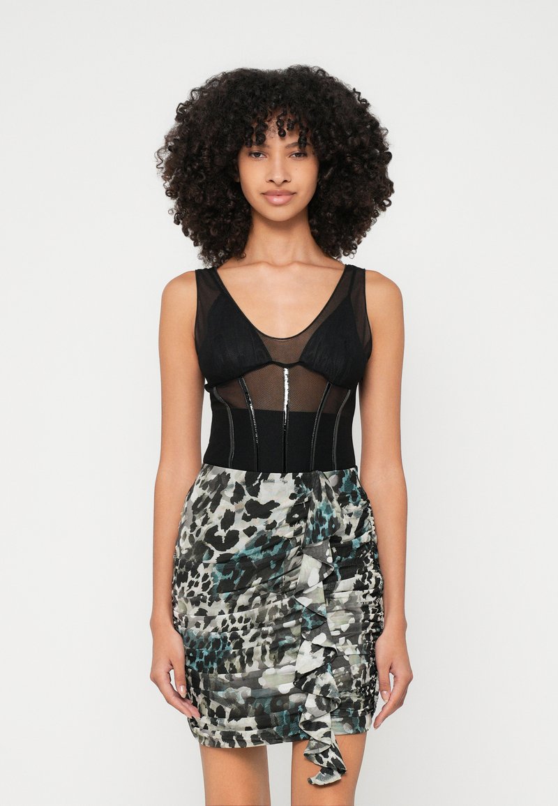 Crni mrežasti bodysuit s dubokim V-izrezom; uparen s mini suknjom raznih boja s uzorkom koja ima volančiće i prilagođeni kroj.