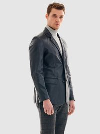 Mörk läderblazer med strukturerad design, spetsiga slag, enkel knappstängning och fickor. Bärs över en ljusgrå polotröja och rutiga byxor.