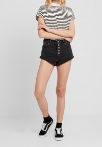 Svarta denimshorts med hög midja och femknappsstängning, rullad kant; tillsammans med en svart och vit randig t-shirt och svarta sneakers.