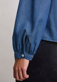 Denimhemd mit langen, gepufften Ärmeln, ausgestattet mit knöpfbaren Manschetten und seitlichen Schlitzen, in einer mittleren blauen Farbe mit glatter Textur.