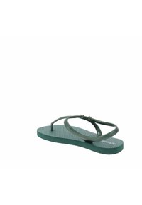 Chanclas verdes con suela texturizada, tiras delgadas trenzadas y acentos decorativos cerca del tobillo. Diseño ligero adecuado para el verano.