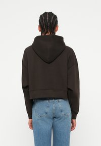 Sweatshirt preto cortado com um capuz amplo e mangas caídas, emparelhado com jeans de cintura alta azul claro com uma textura desgastada.
