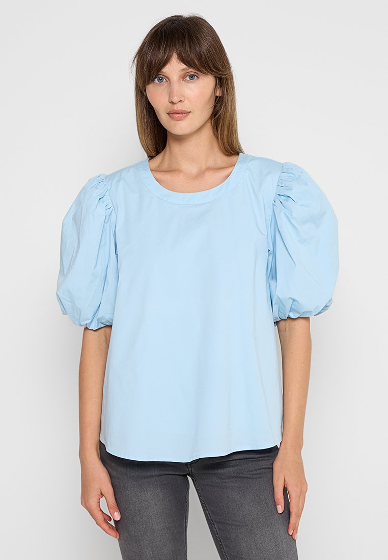 Himmelbluse mit gepufften kurzen Ärmeln, Rundhalsausschnitt und glatter Textur. Getragen mit dunkelgrauen Jeans. Schlichtes und modernes Design.