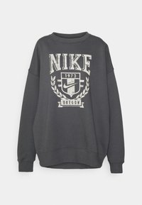 Mörkgrå sweatshirt i bomullsblandning med en stor vit Nike-logotyp och text. Den har rundad halsringning och ribbade muddar.