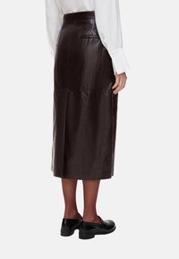 Gonna midi in pelle marrone con vita aderente, texture liscia, dettaglio tasca posteriore e orlo dritto. Indossata con scarpe nere.
