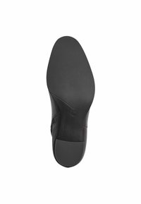 Semelle de chaussure noire avec une surface en caoutchouc texturée, en forme courbée et avec un léger talon. Bord lisse et design minimal sans motifs.