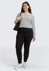 Zwarte hoge taille broek met een pinstripe textuur, gecombineerd met een wit gestreept shirt. Het shirt heeft een ronde halslijn, lange mouwen en casual sneakers.