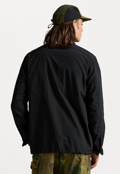 Jachetă neagră ușoară cu mâneci lungi, având un design drept și o textură netedă. Asortată cu pantaloni cargo cu model de camuflaj.
