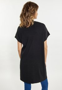 Czarna tunika z krótkim rękawem o luźnym kroju, teksturowanym materiale, zaokrąglonym dole i wysokim dekolcie, zestawiona z niebieskimi skinny jeans.