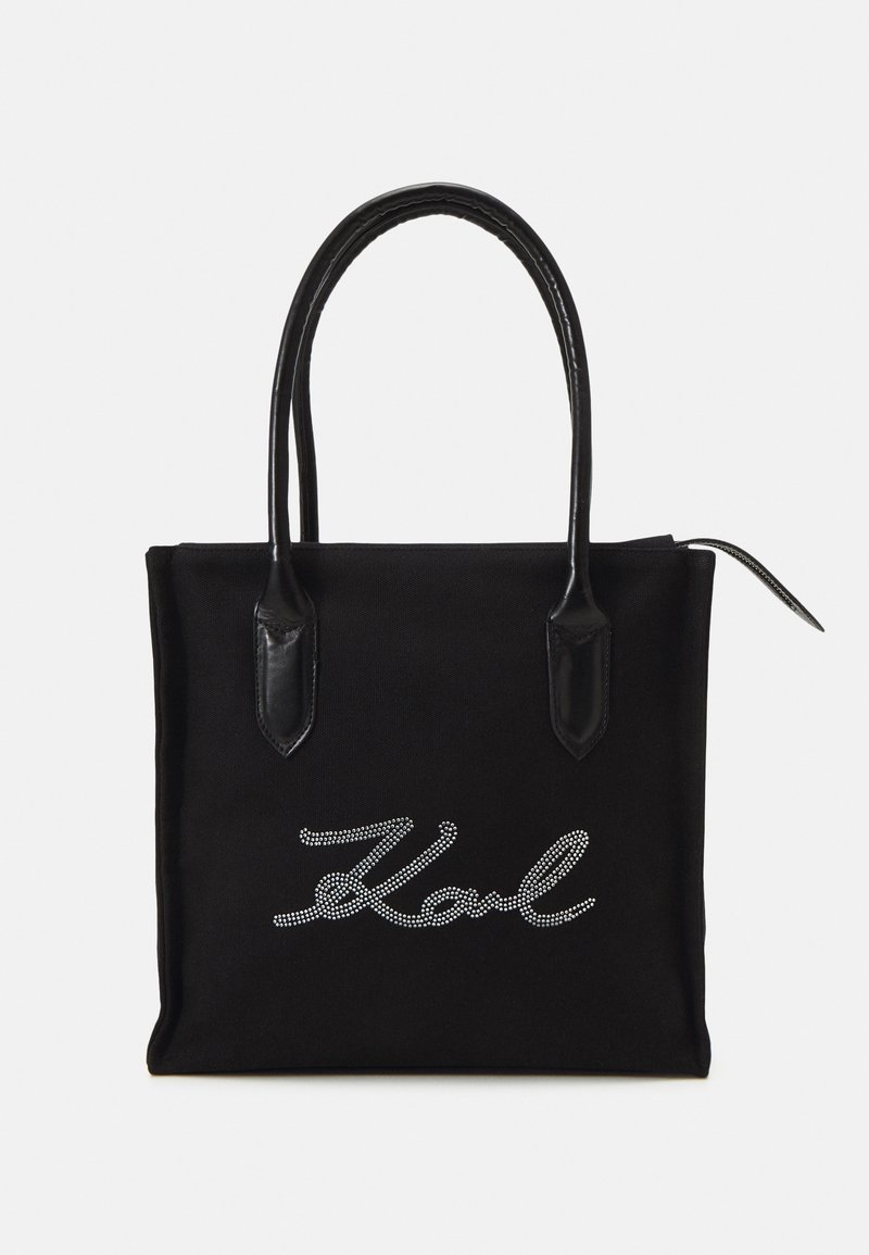 Black canvas tote bag with leather handles, featuring a silver rhinestone 'Karl' logo on the front. Simple rectangular design.