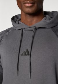 Γκρι φούτερ με κουκούλα, με υφασμάτινες μαύρες λεπτομέρειες στους ώμους, κορδόνια και μαύρο λογότυπο Adidas στο στήθος. Μαλακό ύφασμα.