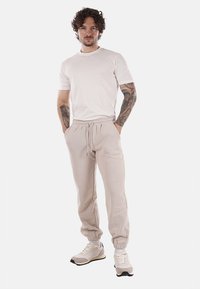 Joggers de algodón beige con cintura elástica, bolsillos frontales y puños en los tobillos, combinados con una camiseta blanca básica y zapatillas beige.