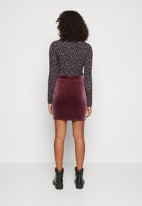 Blusa de manga larga con estampado en tonos oscuros, combinada con una falda corta de terciopelo burdeos y botas negras con suela gruesa. Textura suave y diseño ajustado.