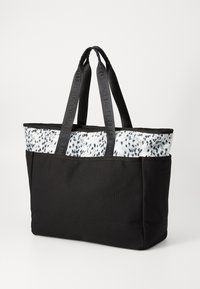 Svart tote bag med en teksturert stoff, har en hvit toppseksjon med svart trykk, og robuste svarte håndtak med preget merkevare.
