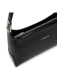Sac en cuir noir avec une texture lisse, fermeture éclair et accents métalliques. Présente un logo embossé à l'avant. Design compact.