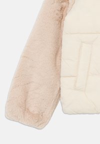 Ermel detalj av en beige jakke som viser mykt, lodden stoff på den ene siden og quiltepolstret stoff med en lomme på den andre siden.