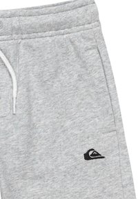 Pantalones de chándal grises hechos de una tela texturizada, con una cintura elástica y cordón ajustable, con un pequeño logo negro en el lado izquierdo.