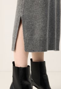 Jupe midi en maille grise avec fente latérale portée avec des bottines en cuir noir sur jambes nues.