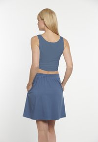 Modrá crop top tank a zodpovedajúca sukňa s vysokým pásom; obe vyrobené z mäkkej, elastickej látky s voľným strihom a elastickým pásom.