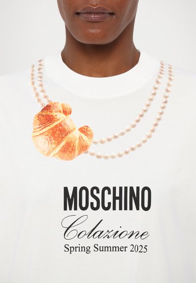 White t-shirt featuring a croissant graphic and pearl necklace print. Text reads "MOSCHINO Colazione Spring Summer 2025" in black.