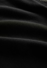 Fekete anyag sima textúrával, finom redőkkel és matt felülettel. Nincsenek látványos minták vagy fémrészek.