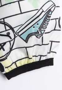 Los pantalones cortos gráficos presentan una tela blanca con patrones de líneas negras, ilustraciones de zapatillas deportivas azules y una cinturilla elástica negra.