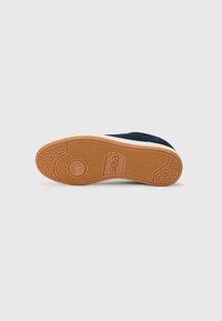 Shoe sole with a textured rubber design, featuring a gum color with an embossed logo and herringbone pattern for traction.