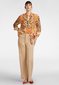 Camicia a maniche lunghe con stampa floreale e stampa leopardata in arancione, rosa e beige, abbinata a pantaloni beige a gamba larga con una cravatta a fantasia. Scarpe arancioni.