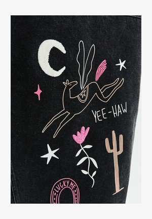 Abstrakcyjny kontur konia z skrzydłami, półksiężycem, gwiazdami, różowym kwiatem, kaktusem i napisem „YEE-HAW” na ciemnym tle materiału.