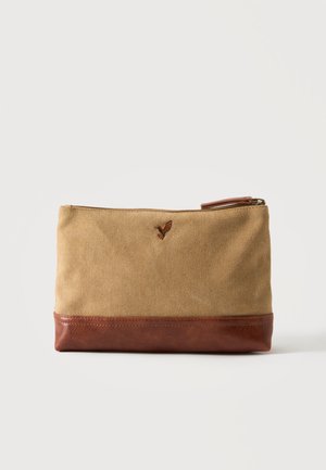Bolsa de lona beige con base de cuero marrón y cremallera, con una pequeña mariposa bordada cerca del centro superior.