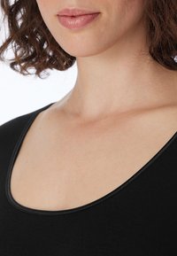 Schwarzes Top mit Rundhalsausschnitt aus weichem Stoff mit glatter Textur. Verfügt über eine kontrastierende Naht entlang des Ausschnitts und der Schulter.