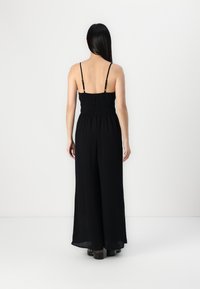Macacão preto sem mangas com corpete franzido, pernas largas e alças ajustáveis. Tecido suave e leve com um design minimalista.