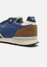 Tenisky s modrým nylonovým svrškem, hnědým semišovým patkem, bílými akcenty a černou gumovou podrážkou. Na straně je logo "Pepe Jeans".