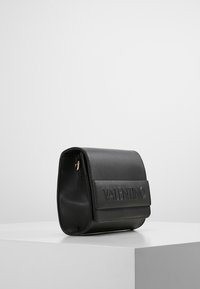 Borsa a tracolla in pelle nera con forma strutturata, logo impresso sul fronte, accessori dorati e chiusura a patta. Texture liscia e design minimalista.