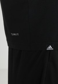 Svart träningsskjorta med texten 'CLIMALITE', korta ärmar och en logotags. Mjuk bomullstyg, avslappnad passform och slät textur.