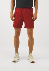Rote Sportshorts mit elastischem Taillenbund und seitlichen Taschen, mit einem Logo am linken Saum. Glattes Material und knielange Passform.