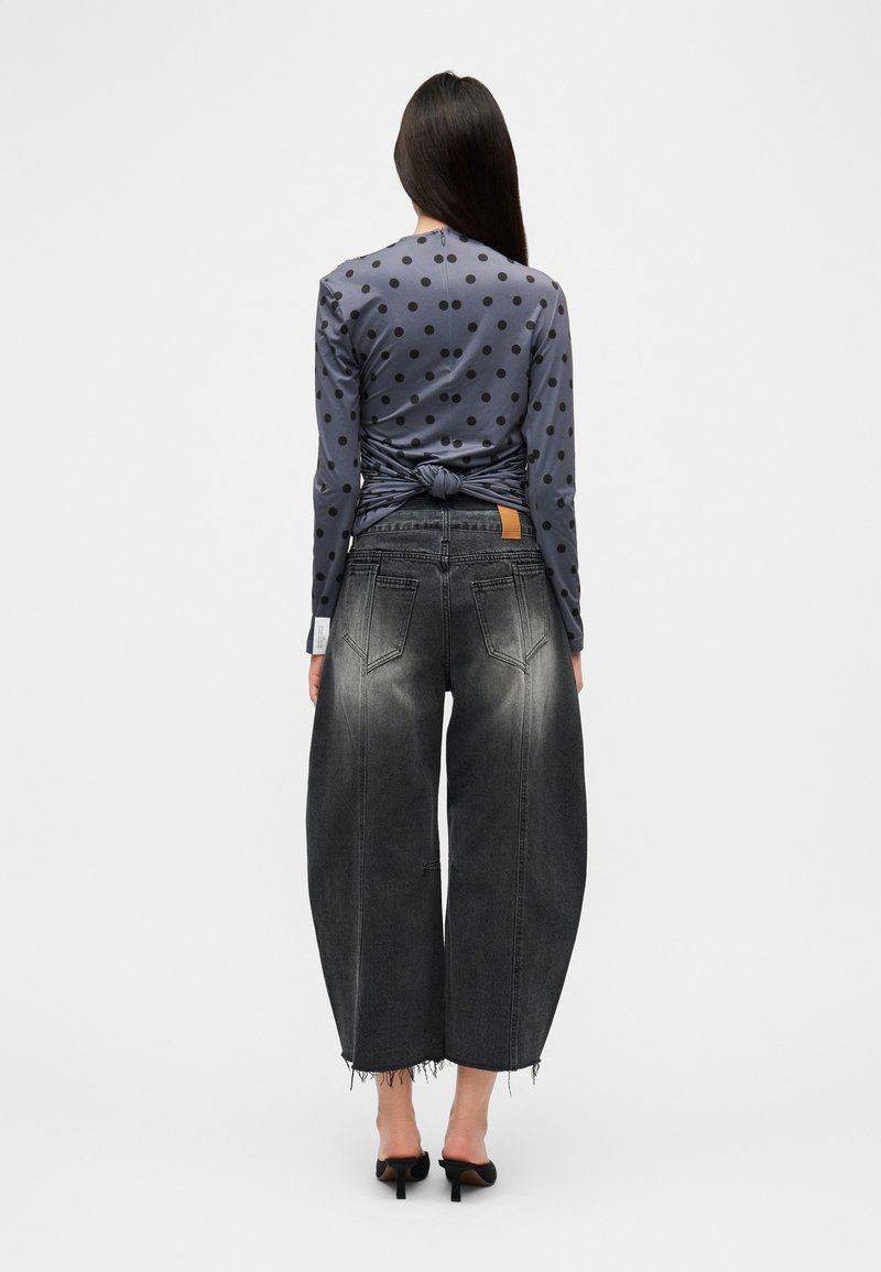 Haut à manches longues gris à pois avec détail noué dans le dos, associé à un jean noir taille haute, jambe large, avec effet délavé à l'avant et ourlet effiloché.